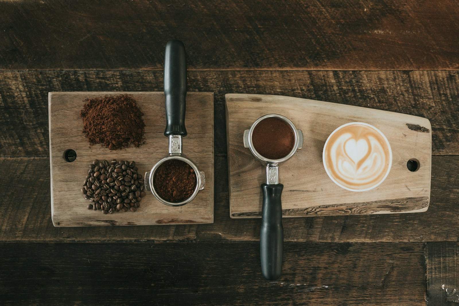 Espresso portafilters, ground coffee, beans and a latte on a wooden board